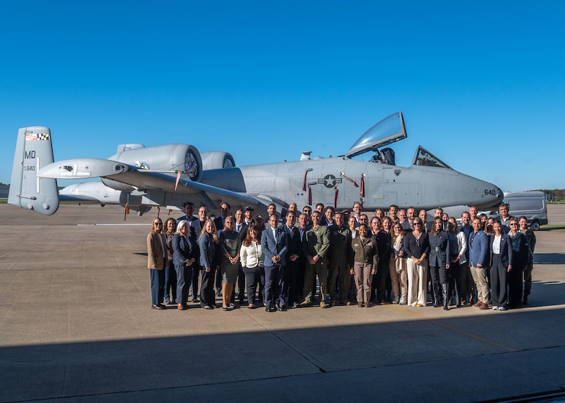 A group of people pose for a photo in front of a military aircraft.