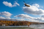 A CH-47 Chinook helicopter belonging to the Connecticut National Guard's 169th Aviation Regiment prepares to gather water from a local lake to dump on a brushfire burning on Lamentation Mountain in Berlin, Connecticut Oct. 23, 2024. This was the first time since 1995 that Connecticut National Guard aviation units conducted an aerial firefighting mission in state.