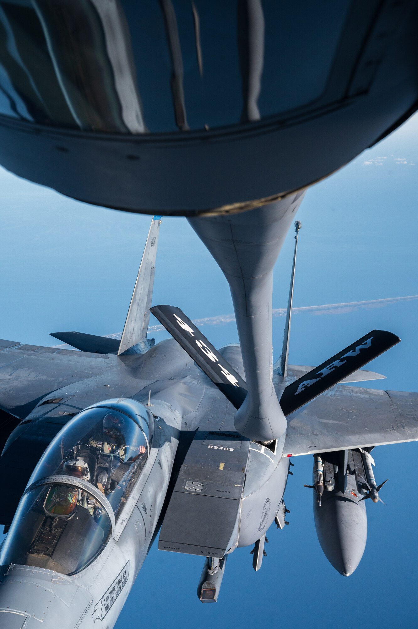 A military jet refuels another while in flight. The boom tail of the tanker reads "434 ARW". Two pilots are visible in the cockpit of the recipient jet.