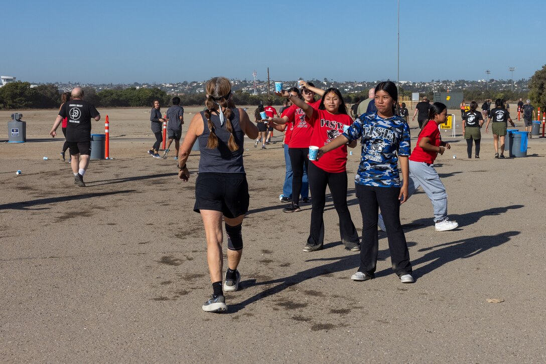 Volunteers hand out water during the 2024 Marine Corps Recruit Depot Boot Camp Challenge, Oct. 19, 2024. For the past 23 years, MCRD San Diego has hosted the bootcamp Challenge, a three-mile obstacle course race guided by 60 drill instructors that highlights the physical and mental demands of bootcamp. The event fosters camaraderie and community engagement through interaction with MCRD personnel.