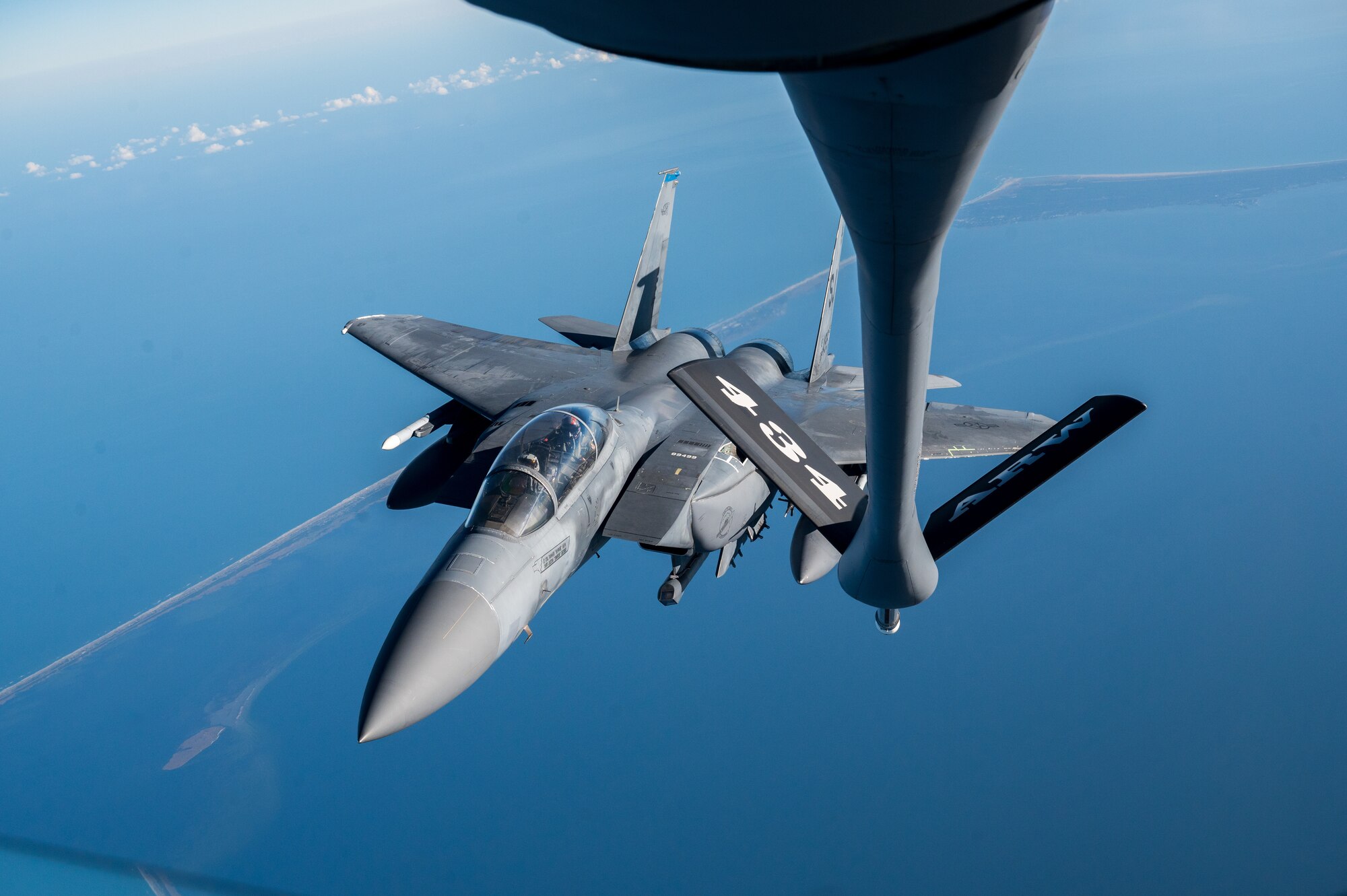 A military aircraft flies over a visible coastline, few clouds visible. Next to it, the boom arm of another military aircraft. The boom reads "434 ARW".