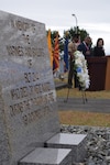 A memorial marker in honor of the fallen is in the foreground, while a speaker stands in the background, addressing an audience.
