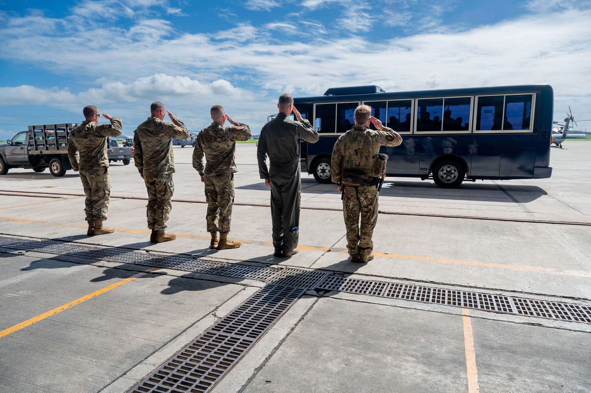 Military members salute a bus with the commander inside the bus as it drives away