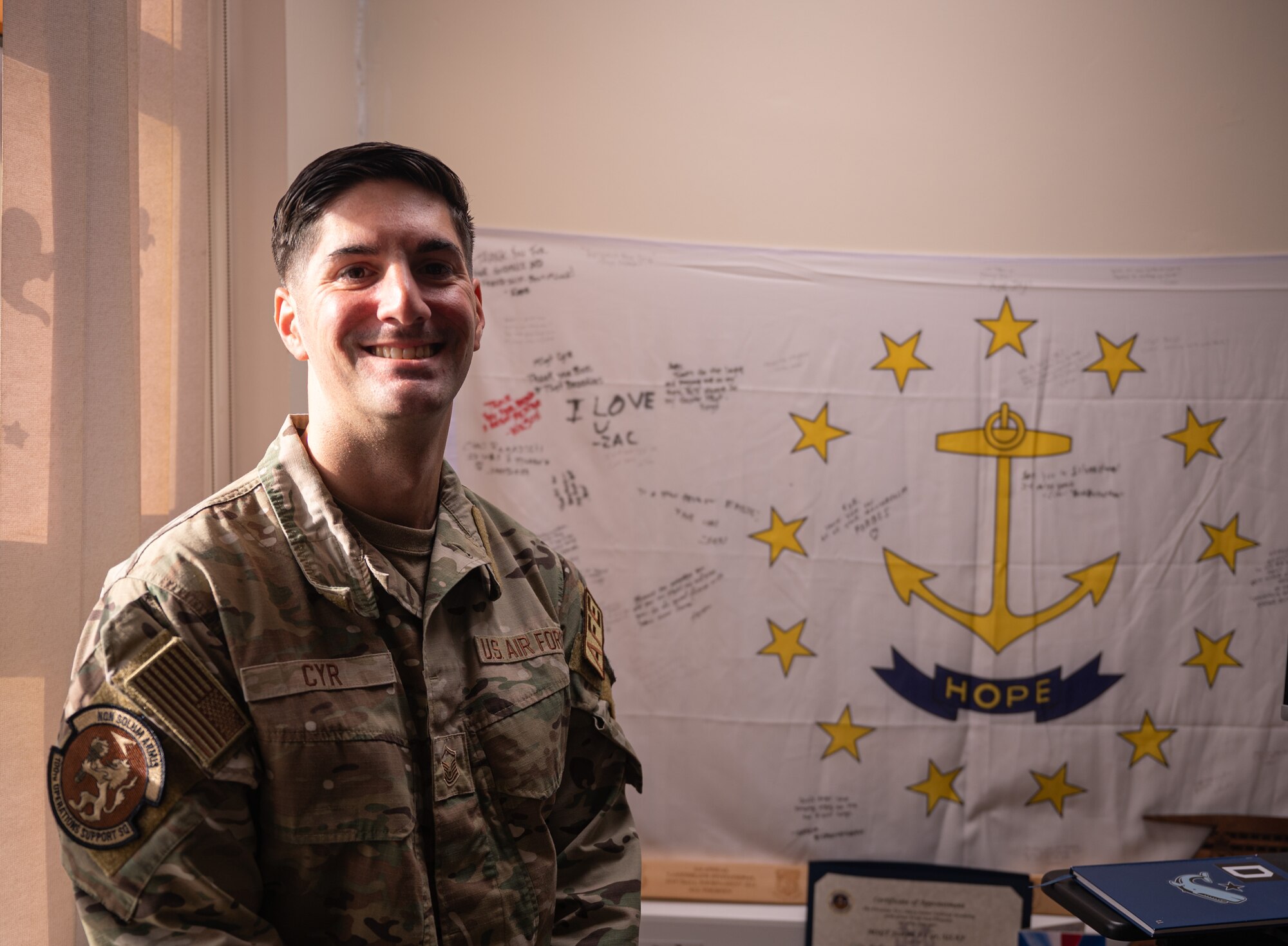 U.S. Air Force Master Sgt. Joseph Cyr, 100th Operations Support Squadron Aircrew Flight Equipment superintendent, stands in front of a signed flag from his U.S. Navy Senior Enlisted Academy class inside his office at Royal Air Force Mildenhall, England, Oct. 22, 2024.