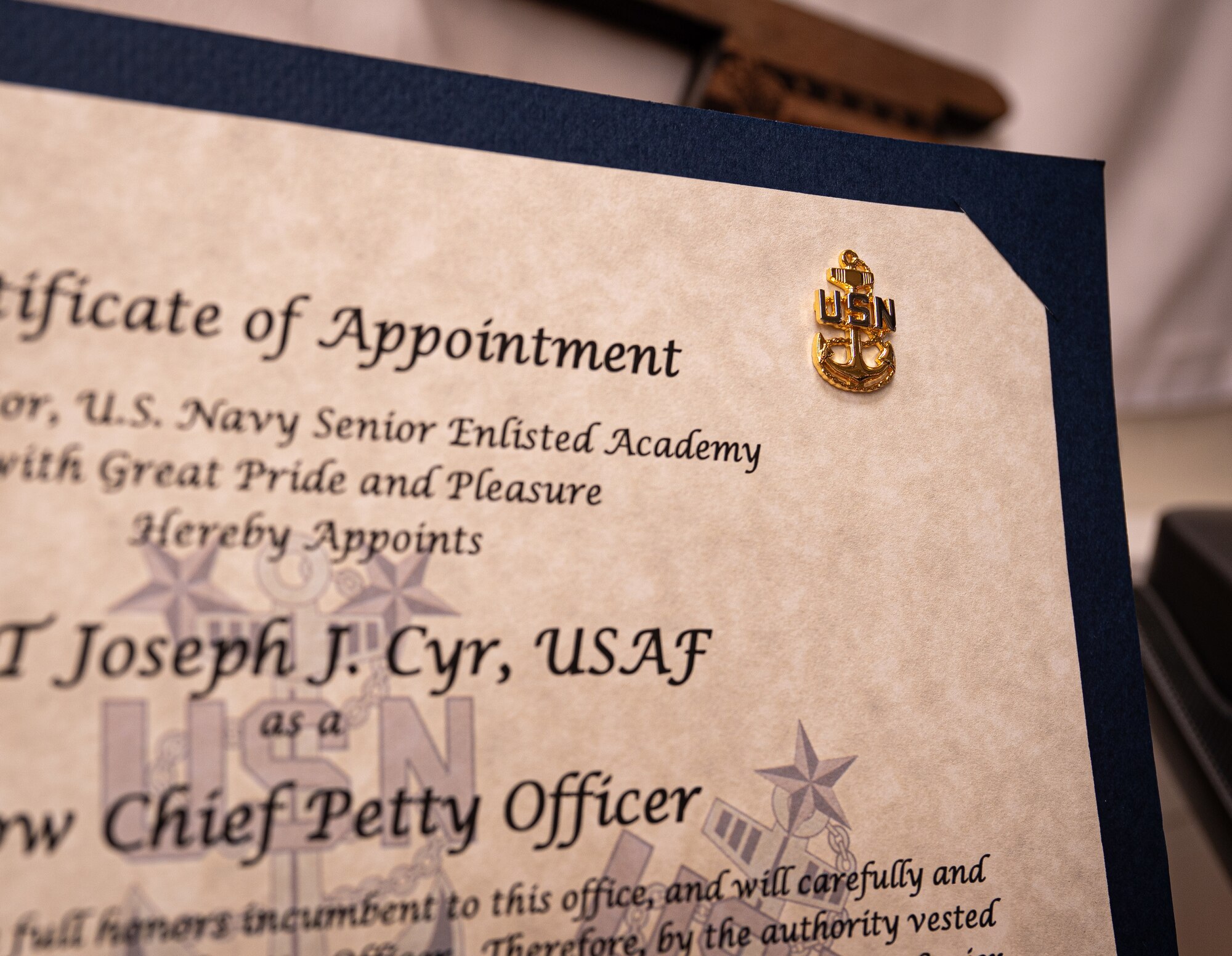 The Fouled Anchor, an emblem of the rate of chief petty officer of the U.S. Navy, is pinned on a certificate for U.S. Air Force Master Sgt. Joseph Cyr, 100th Operations Support Squadron Aircrew Flight Equipment superintendent, at Royal Air Force Mildenhall, England, Oct. 22, 2024.