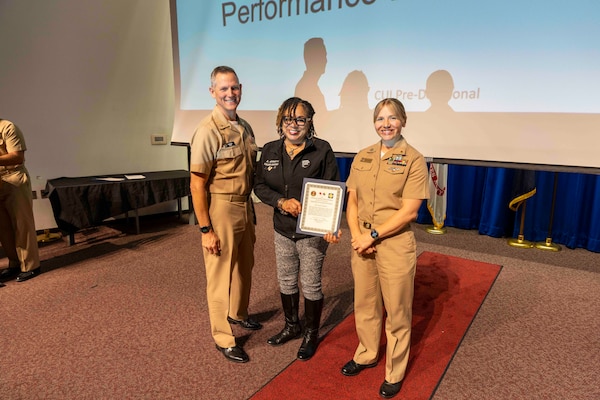 241010-JC800-1020 BETHESDA, Md. (Oct. 10, 2024) - Capt. William Deniston, lead inspector for the Medical Inspector General, awards a certificate of recognition to Lt. Jessica Wentlent and Ms. Alexa Garrett, program managers for the performance evaluation system,  during an out brief for MEDIG. (U.S. Navy Photo by Mass Communication Specialist 1st Class Heath Zeigler)