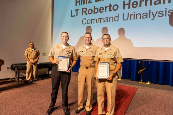 241010-JC800-1026 BETHESDA, Md. (Oct. 10, 2024) - Capt. William Deniston, lead inspector for the Medical Inspector General, awards a certificate of recognition to Hospital Corpsman 2nd Class Zachary Shedd and Lt. Roberto Hernandez, managers of the urinalysis program, during an out brief for MEDIG. (U.S. Navy Photo by Mass Communication Specialist 1st Class Heath Zeigler)