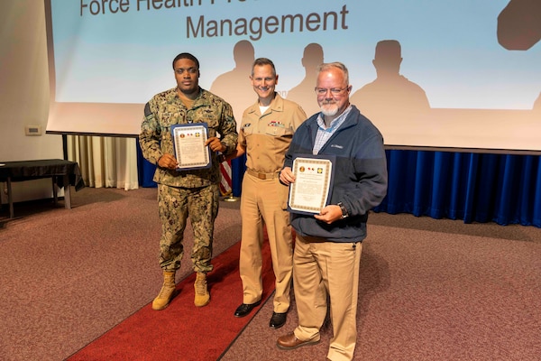 241010-JC800-1029 BETHESDA, Md. (Oct. 10, 2024) - Capt. William Deniston, lead inspector for the Medical Inspector General, awards a certificate of recognition to Hospital Corpsman 1st Class Tylus Charles and Mr. Charles Walton, managers of the emergency management program, during an out brief for MEDIG. (U.S. Navy Photo by Mass Communication Specialist 1st Class Heath Zeigler)