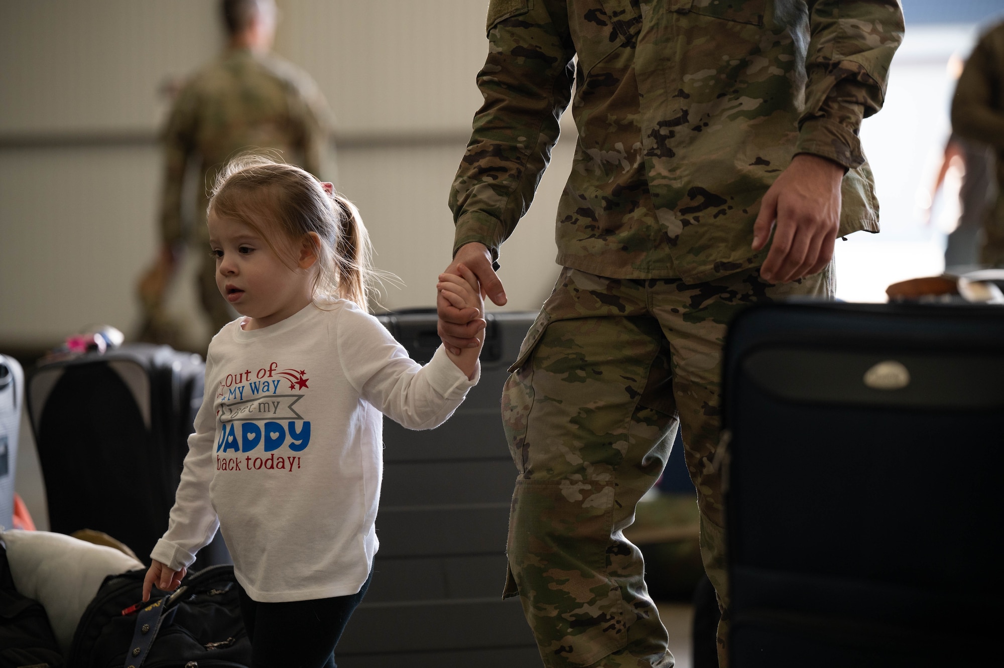A young girl holds the hands of a servicemember as they walk.