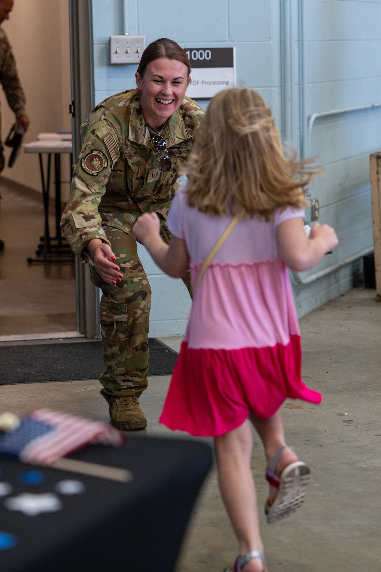 A woman in a military uniform extends her arms as a girl in a dress runs towards her.