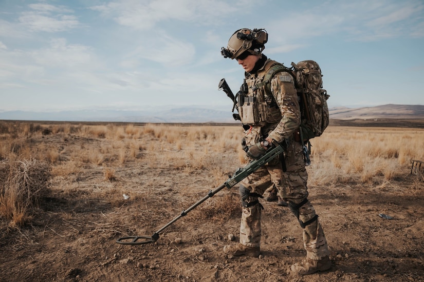 A bomb expert searches for bombs in a field using a metal detector.