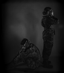 A man crouches with hands over ears while a woman stands with hands over her mouth. The photo is black and white