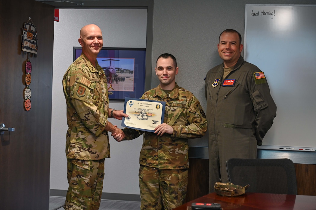 U.S. Air Force Col. Jeff Marshall, 97th Air Mobility Wing (AMW) commander, and Chief Master Sgt. Justin Brundage, 97th AMW command chief award Senior Airman Garrett Royce, 58th Airlift Squadron instructor loadmaster, a certificate for being the Sept. Airmen of the Month, at Altus Air Force Base, Oklahoma, Oct. 28, 2024. Royce enjoys the numerous travel opportunities around the world that come with his Air Force career. (U.S. Air Force photo by Airman 1st Class Lauren Torres)