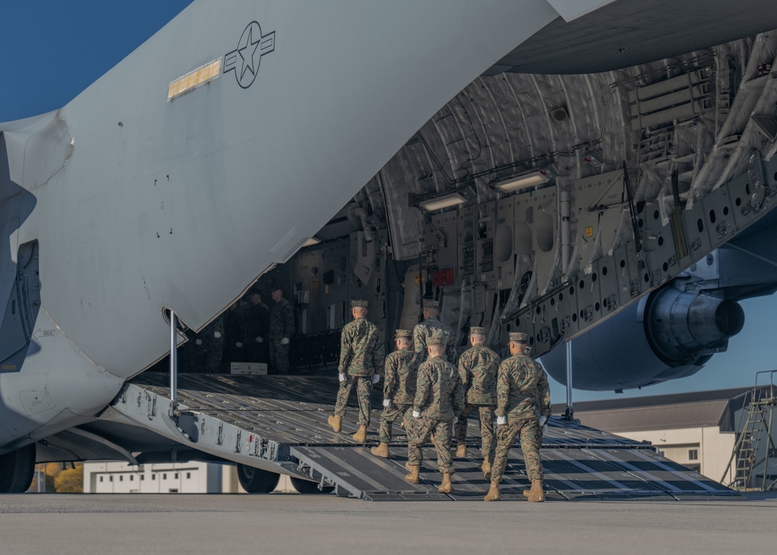A group of Marines marches of the ramp of an aircraft.