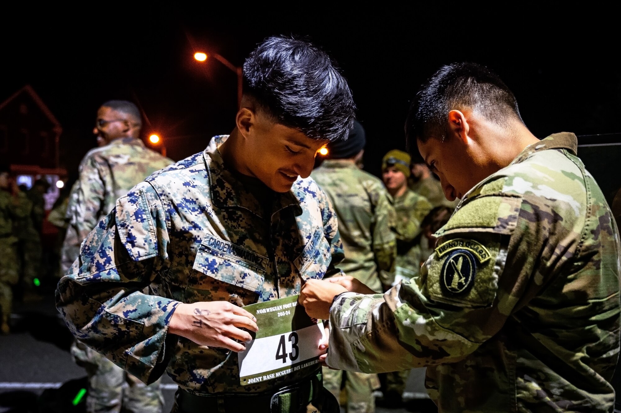 U.S. Army Sgt. Cole Cardenas-Martinez, 174th Infantry Brigade infantryman and U.S. Marine Corps Lance Cpl. Juan Cardenas-Martinez, 1st Marine Corps District infantry rifleman, apply competitor numbers during the Norwegian Foot March at JB MDL, N.J., Oct. 13, 2024. The Norwegian Foot March is a military endurance test where participants march or run an 18.6-mile-long route, carrying a rucksack of 24 lbs. (U.S. Air Force photo by Senior Airman Matt Porter)