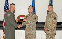 U.S. Air Force Col. Dane J. Gehrmann, left, commander of the Nevada Test and Training Range (NTTR), and Senior Master Sgt. Dennis Kolesnik, right, senior enlisted leader assigned to NTTR, present the Volunteer of the Quarter award to Capt. Yoon Kim, a project manager assigned to NTTR during a commander’s call at Nellis Air Force Base, Nevada, Oct. 31, 2024.
