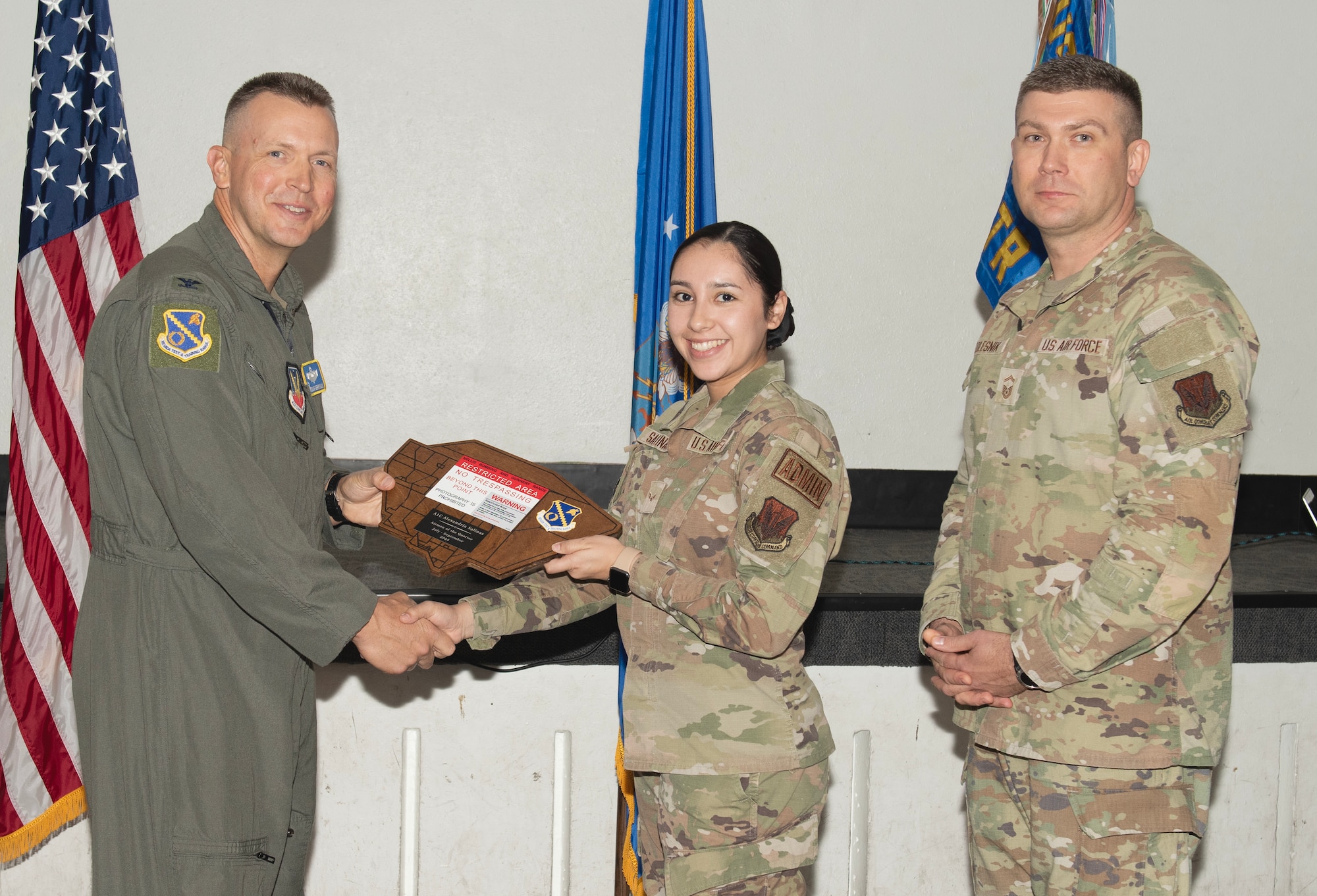 U.S. Air Force Col. Dane J. Gehrmann, left, commander of the Nevada Test and Training Range (NTTR), and Senior Master Sgt. Dennis Kolesnik, right, senior enlisted leader assigned to NTTR, present the Airman of the Quarter to Airman 1st Class Alexandria Salinas, an executive administrator assigned to NTTR during a commander’s call at Nellis Air Force Base, Nevada, Oct. 31, 2024.