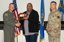 U.S. Air Force Col. Dane J. Gehrmann, left, commander of the Nevada Test and Training Range (NTTR), and Senior Master Sgt. Dennis Kolesnik, right, senior enlisted leader assigned to NTTR, present the Civilian Category II of the Quarter award to Anthony Holmes, a budget analyst assigned to NTTR during a commander’s call at Nellis Air Force Base, Nevada, Oct. 31, 2024.