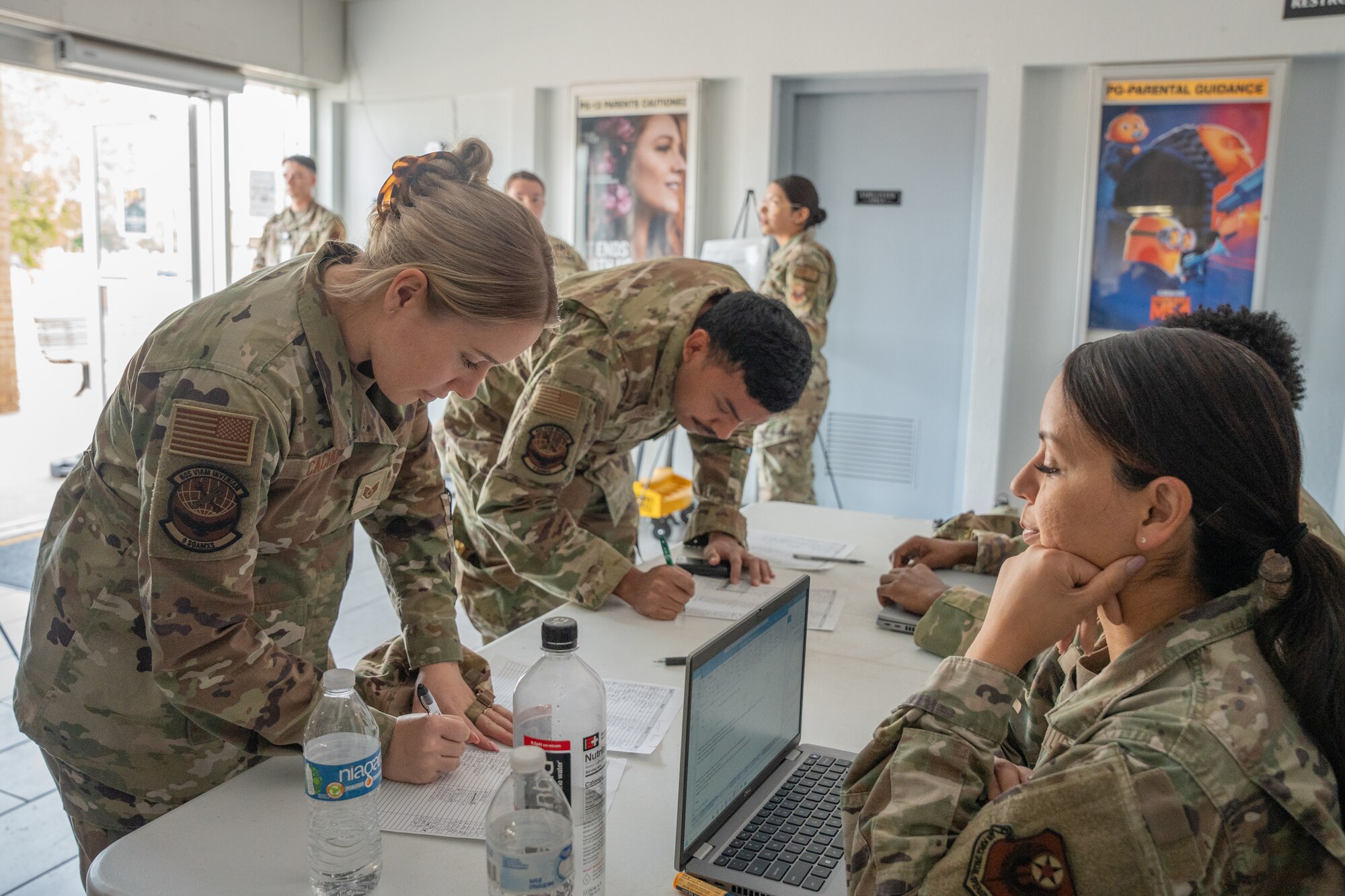 A man and woman in military uniform fill and sign rosters on a table while two individuals in military uniform look on.