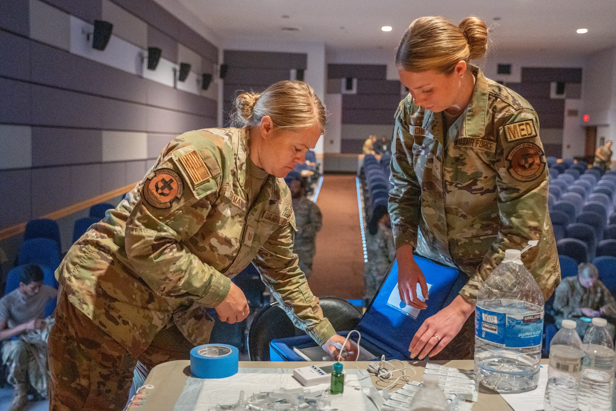 Two women in military uniform handle medical supplies on a table.