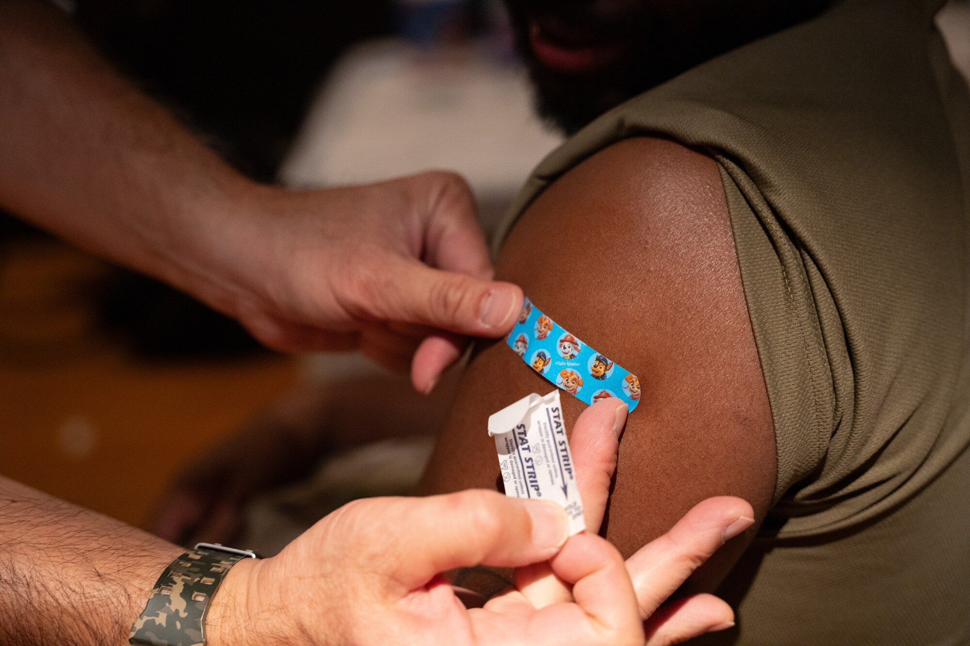 A person puts an adhesive bandage on another person's arm.
