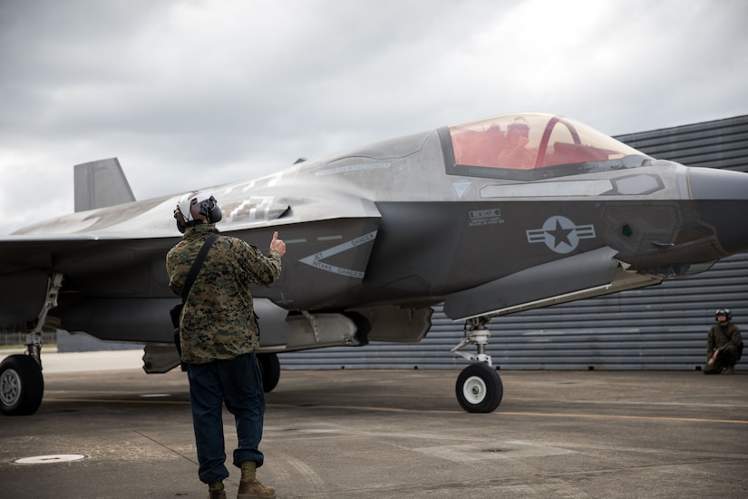 A Marine signals to a jet aircraft on the tarmac.