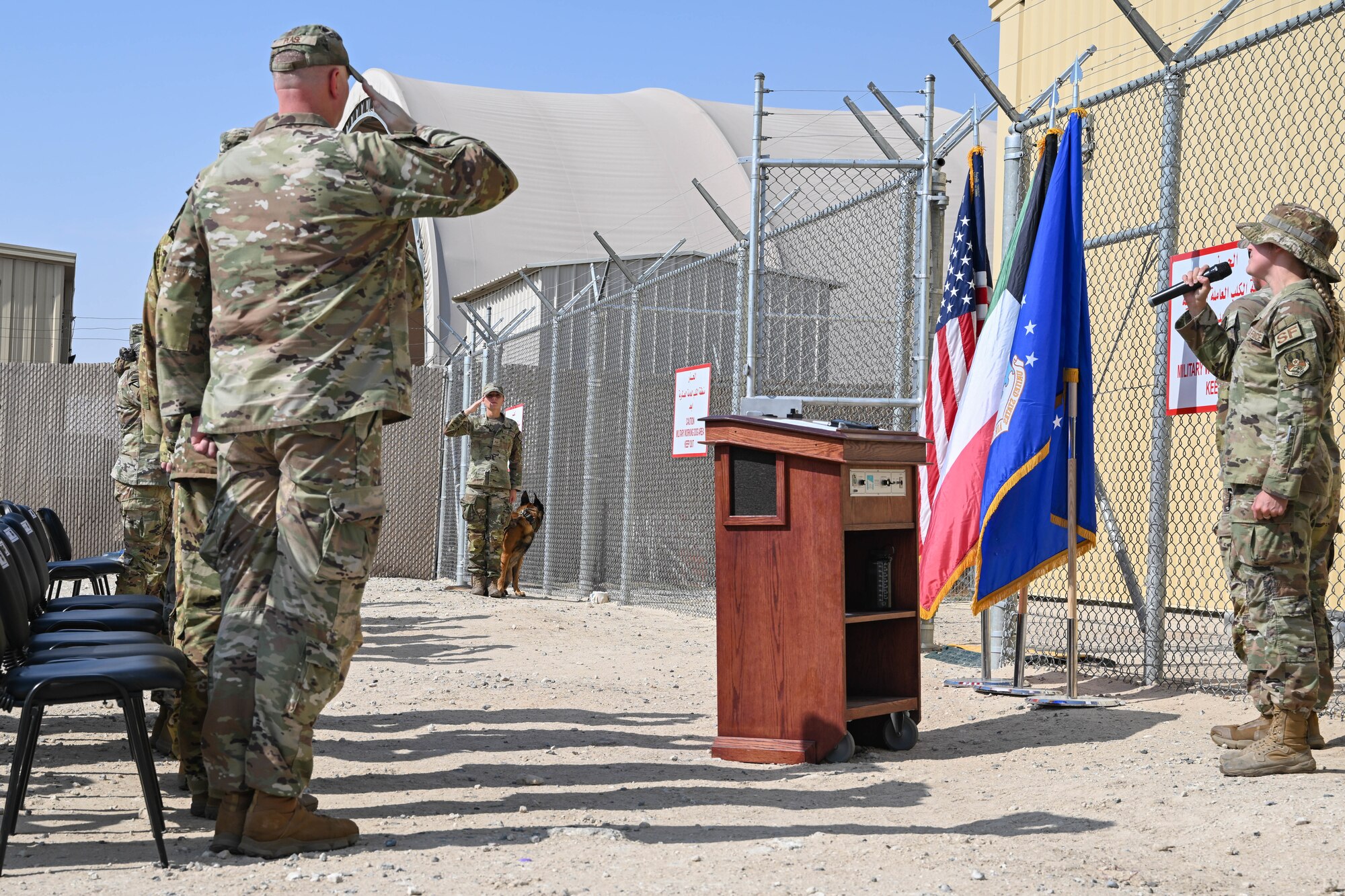 People in uniform salute the American flag.