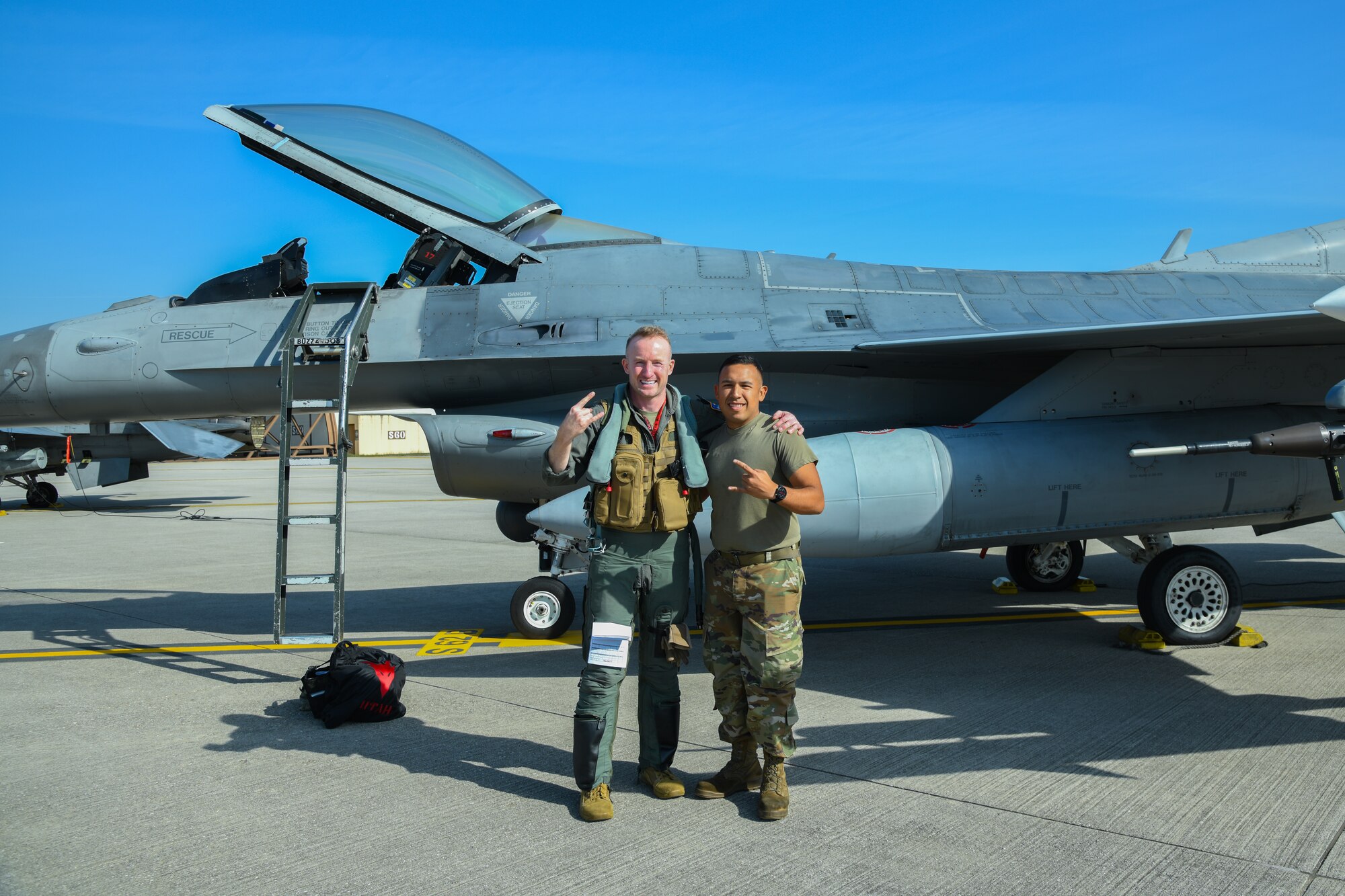 An F-16C pilot and an Airman pose for a photo in front of an F-16C fighter jet