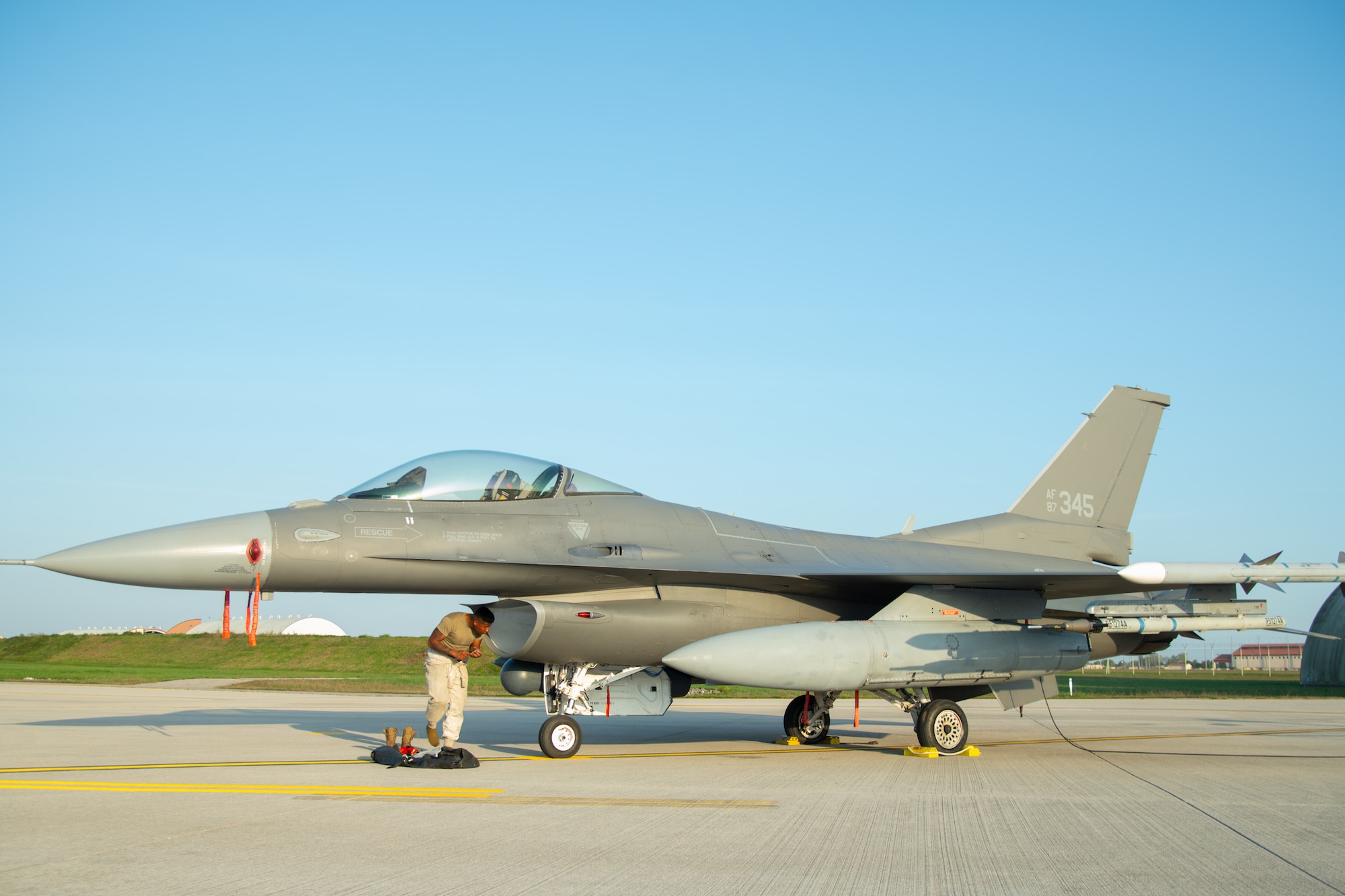 An Airman stands in front an F-16C fighter jet.