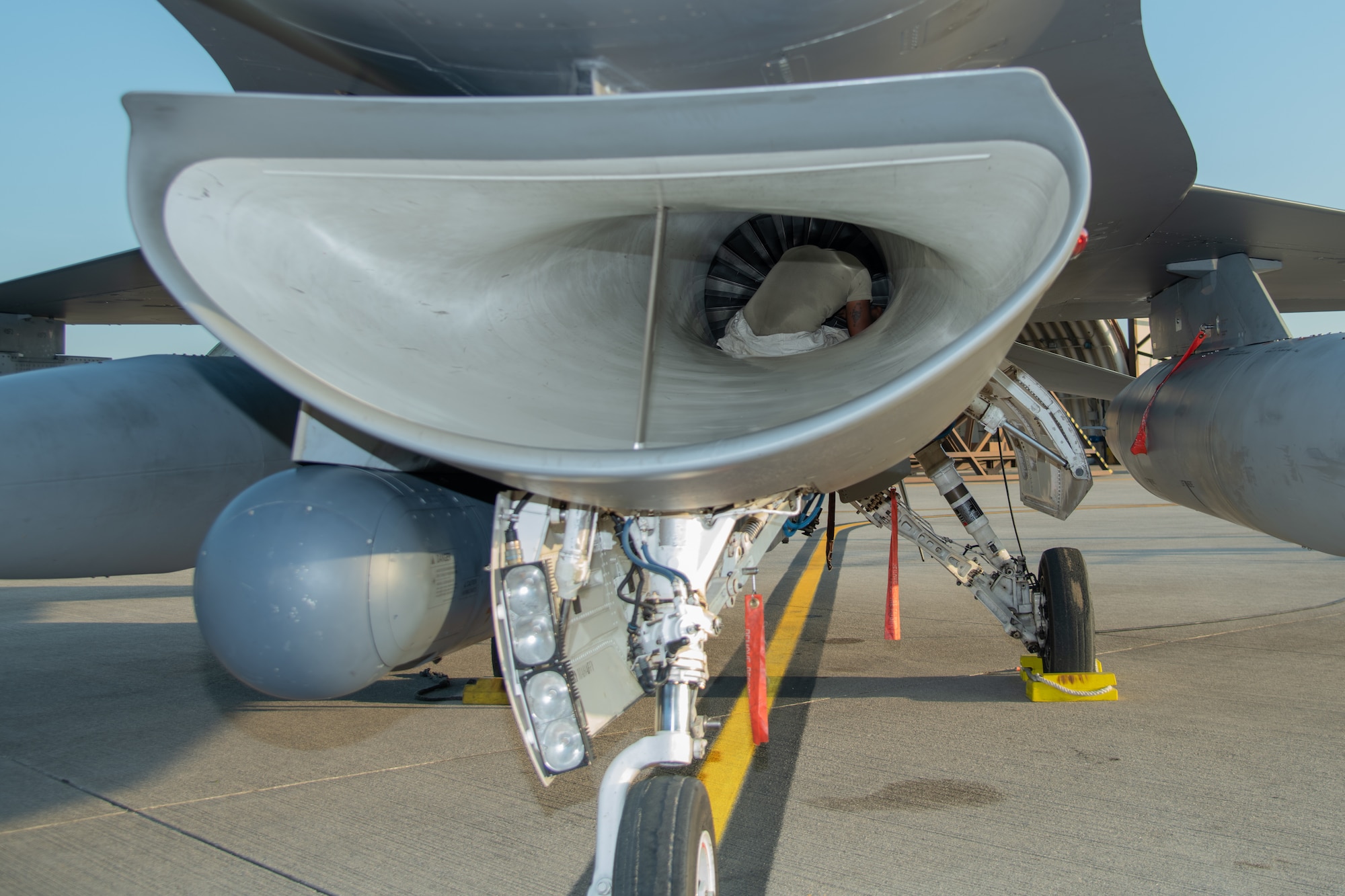 An Airman sits inside the intake of an F-16C fighter jet.