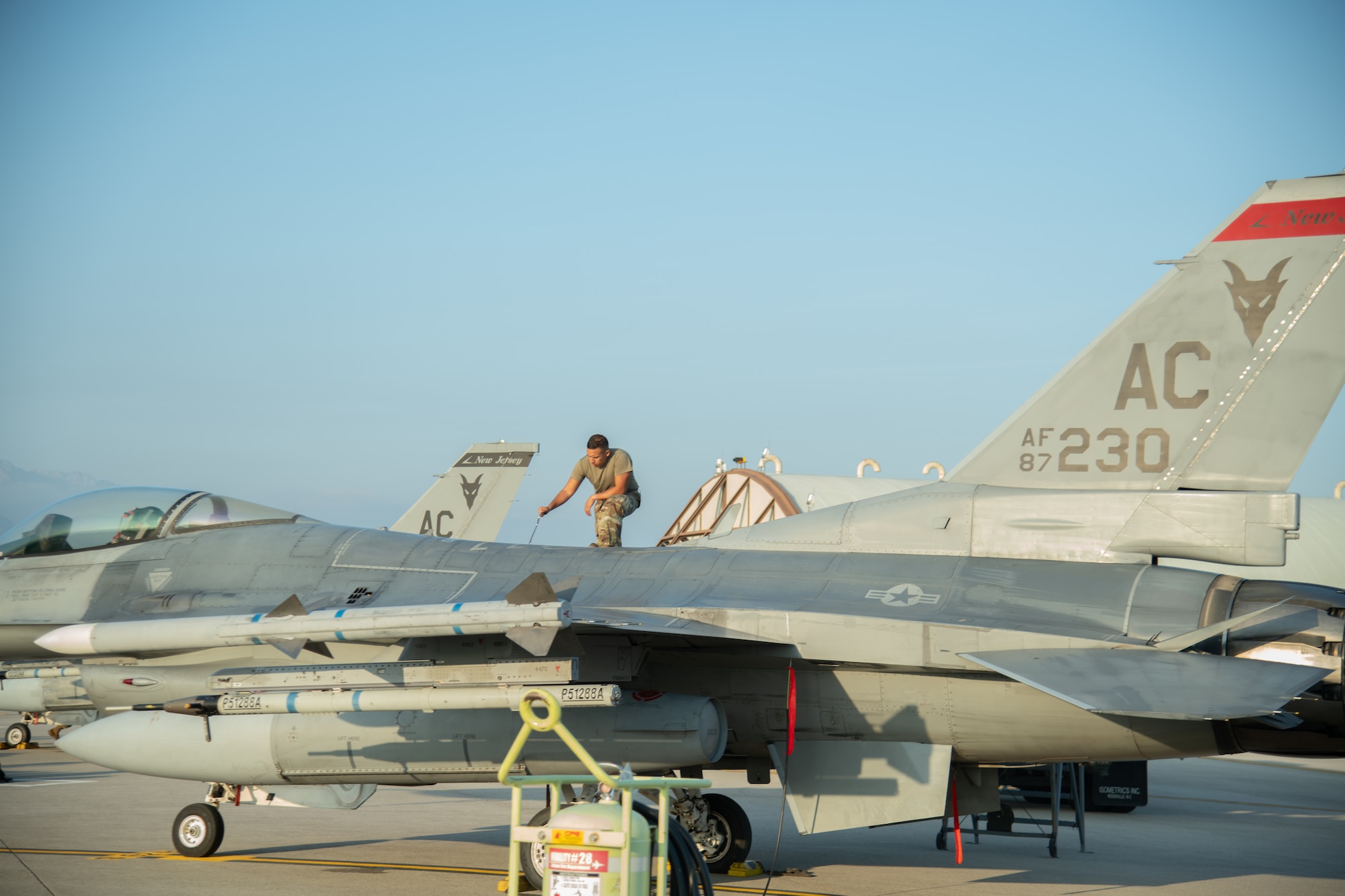 An Airman stands on an F-16C fighter jet while tightening screws.