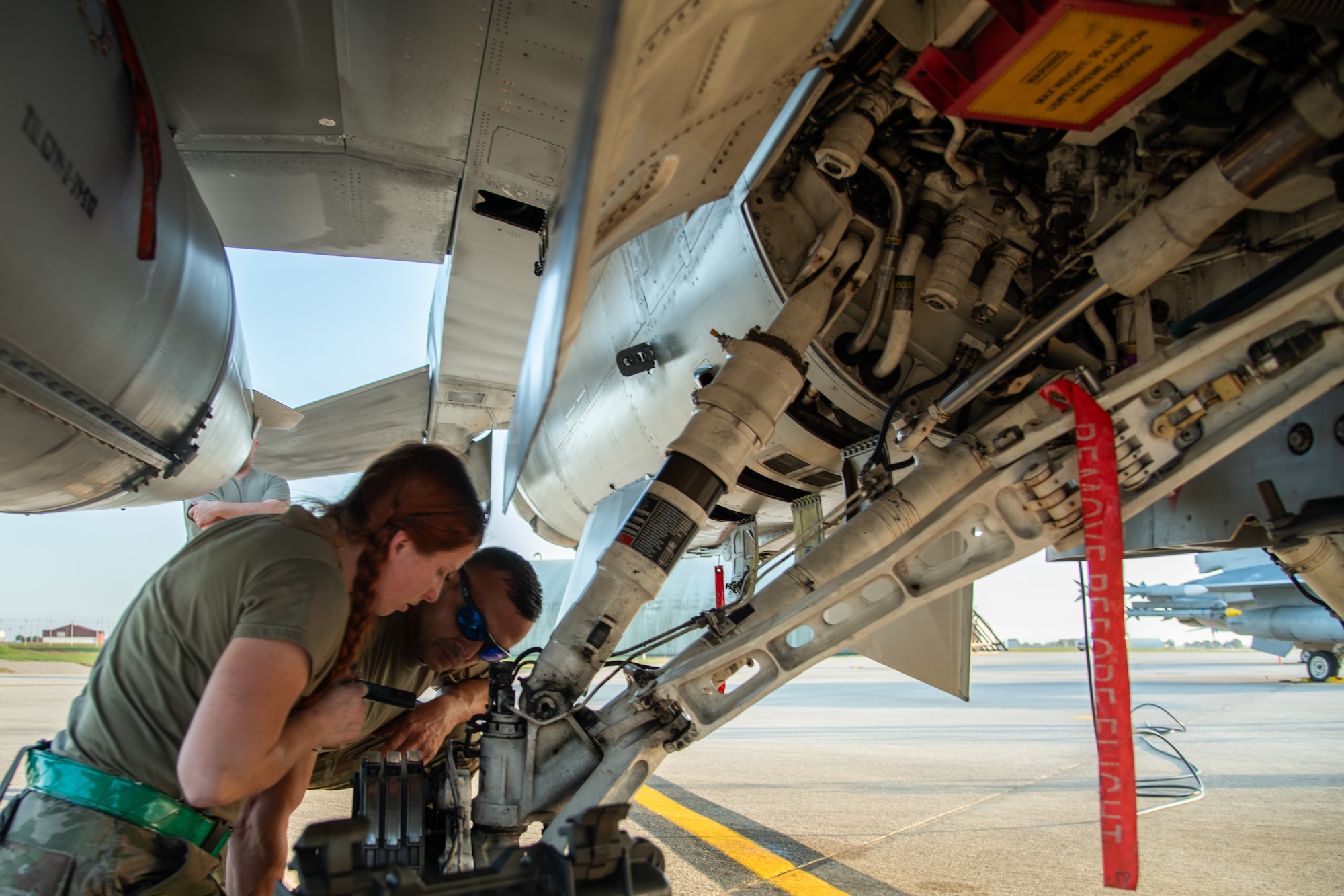 Two Airman change the tire of an F-16C fighter jet.