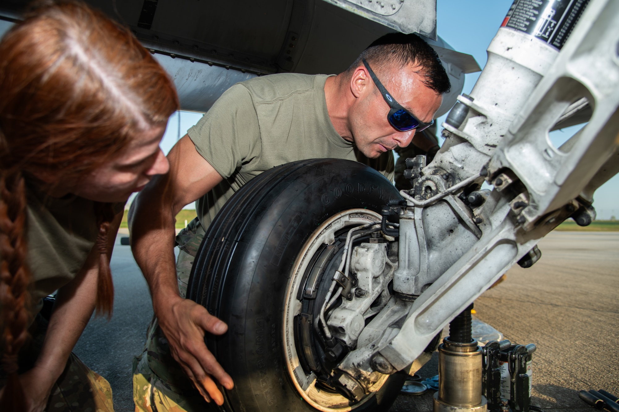 Two Airman change the tire of an F-16C fighter jet.