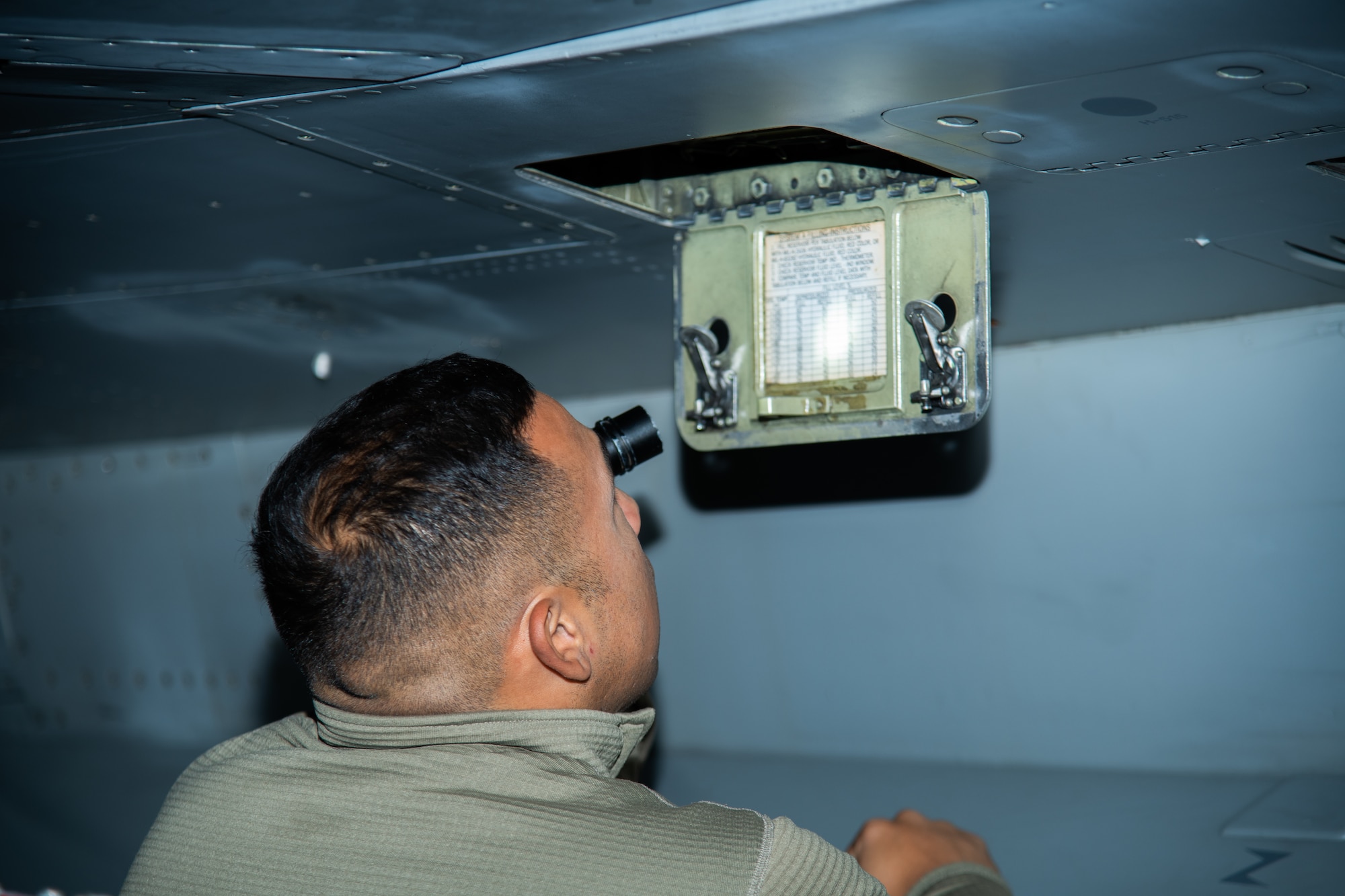 An Airman uses a flashlight to see at night, while conducting an inspection of an F-16C fighter jet.
