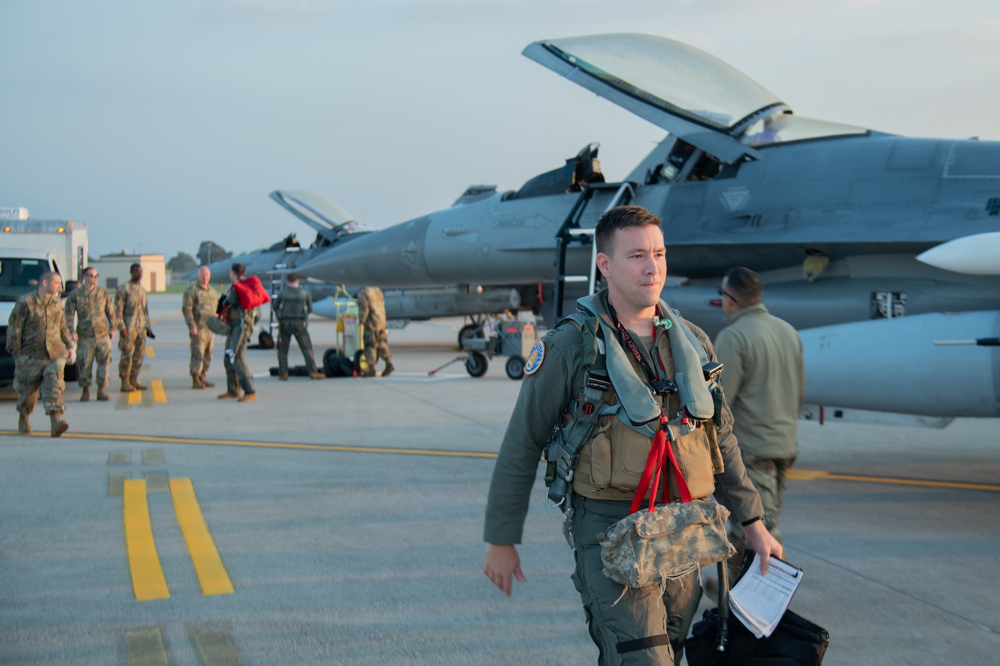 An F-16C pilot walks to his jet with other F-16C fighter jets behind him.
