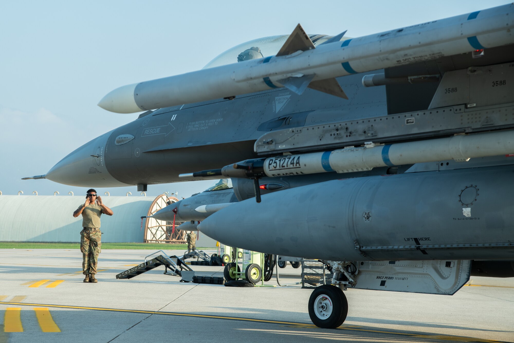 An Airman stands to the side of an F-16C fighter jet with his hands outstretched.