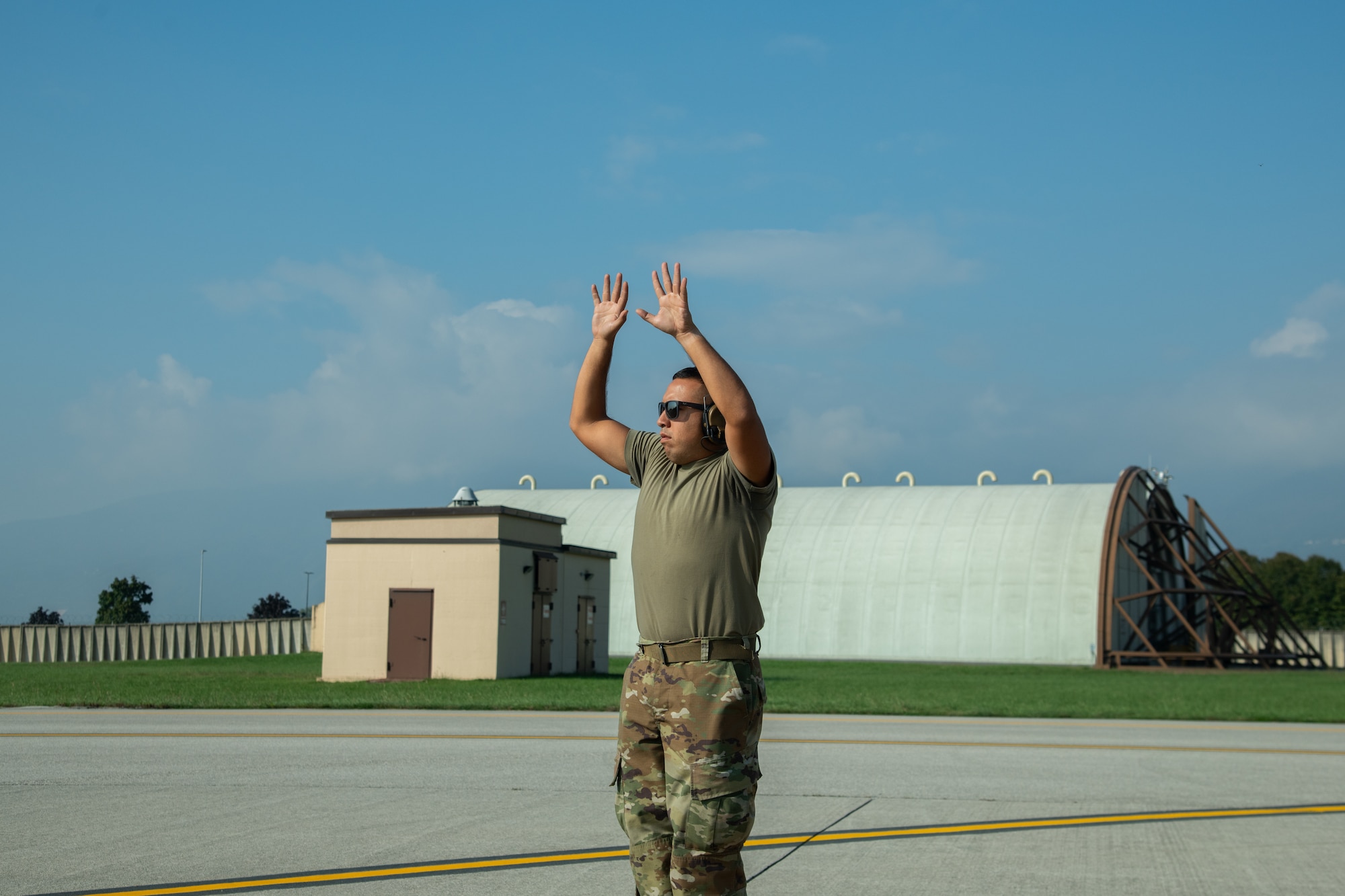 An Airman stands in a flightline with hands raised above his head.