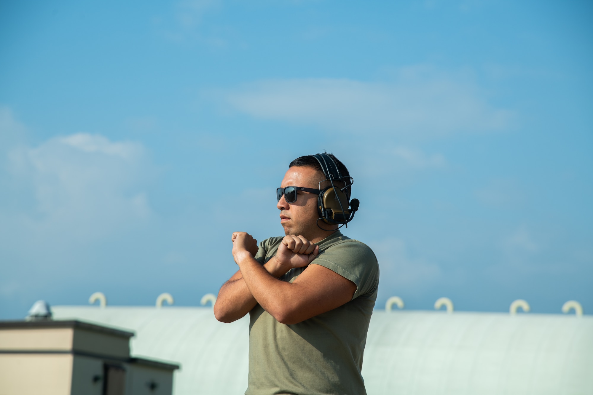 An Airman stands with his arms crossed signaling for an F-16C fighter jet off-photo to stop.