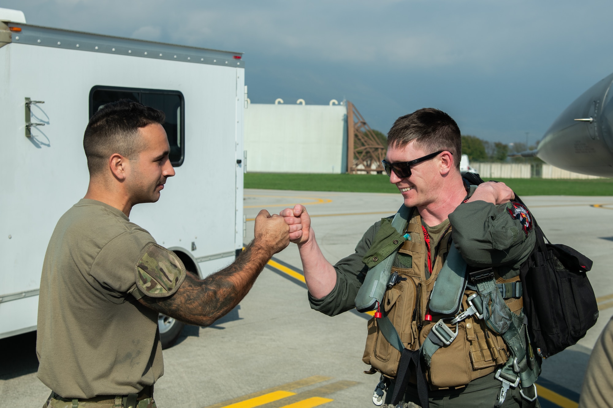 An F-16C pilot and an Airman bump fists next to an F-16C fighter jet.