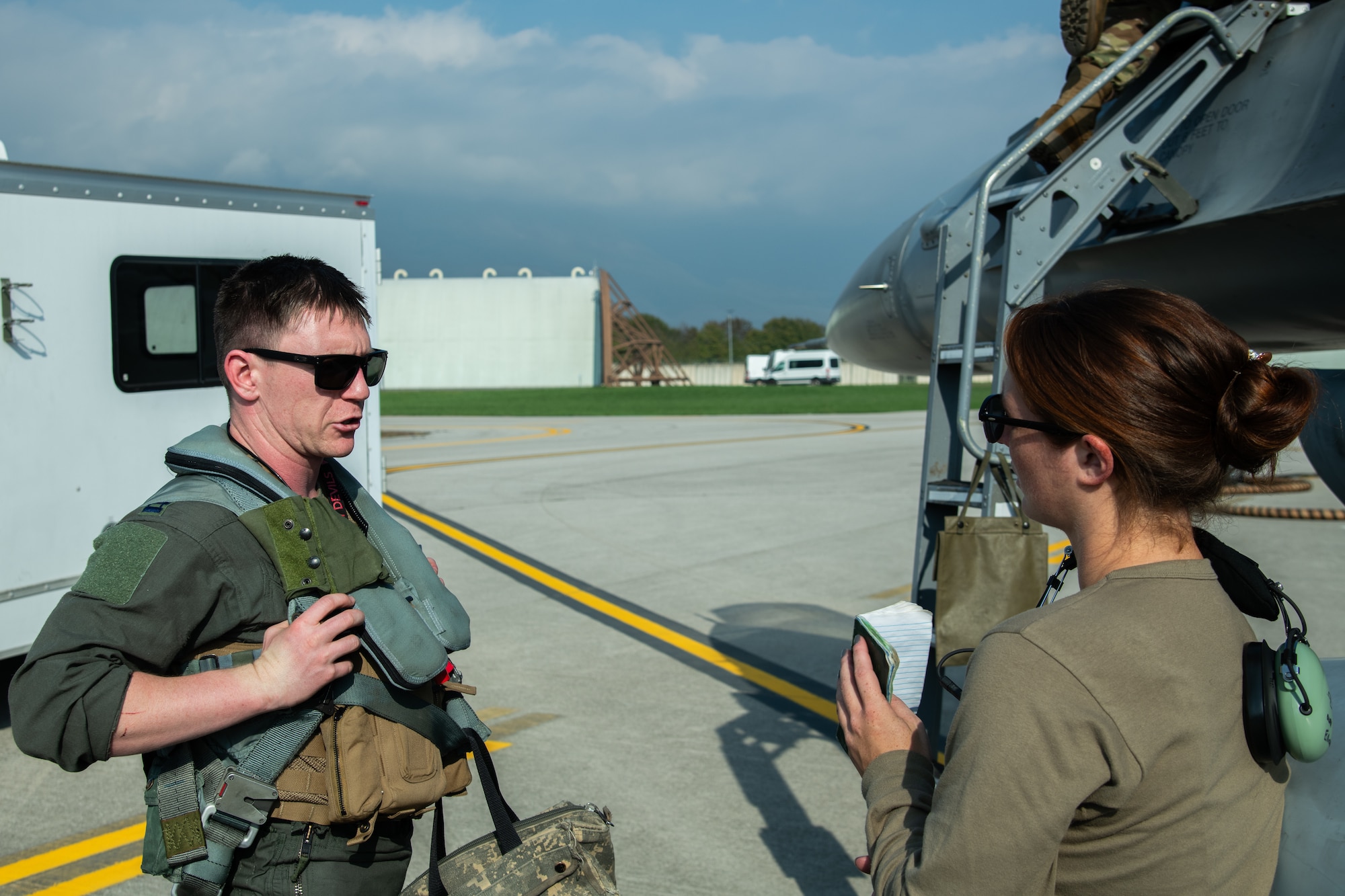 An F-16C pilot speaks to an Airman next to an F-16C fighter jet.