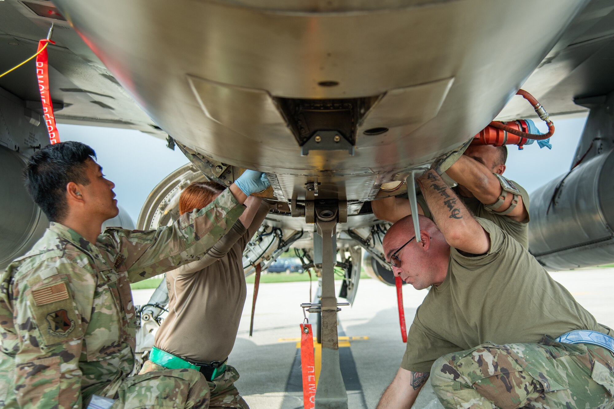 Four aircraft maintainers work underneath an F-16C fighter jet.