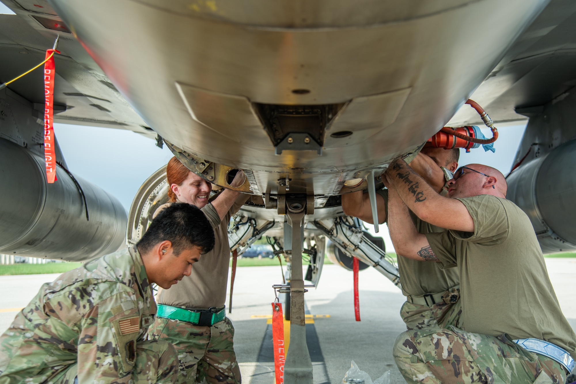 Four aircraft maintainers work underneath an F-16C fighter jet.