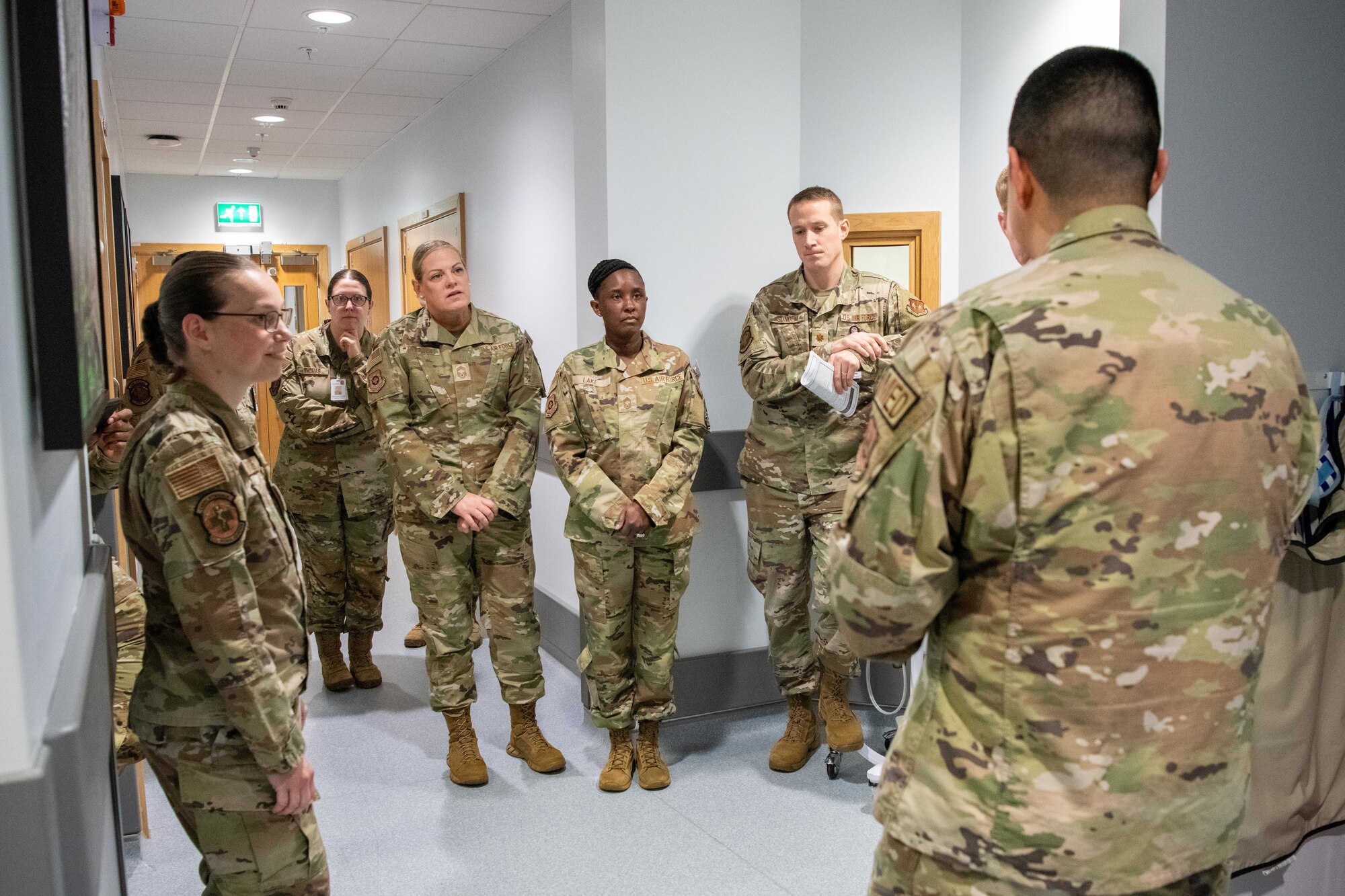 Airmen listen to a brief while standing in a hallway