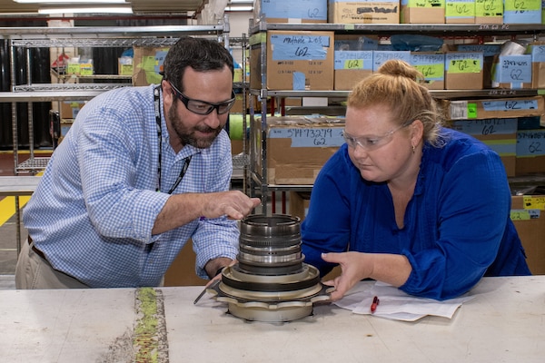 Two people inspect a mechanical part