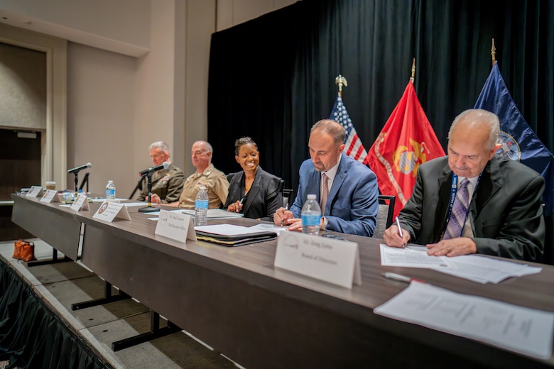 Five people at a long table, signing an agreement on paper.