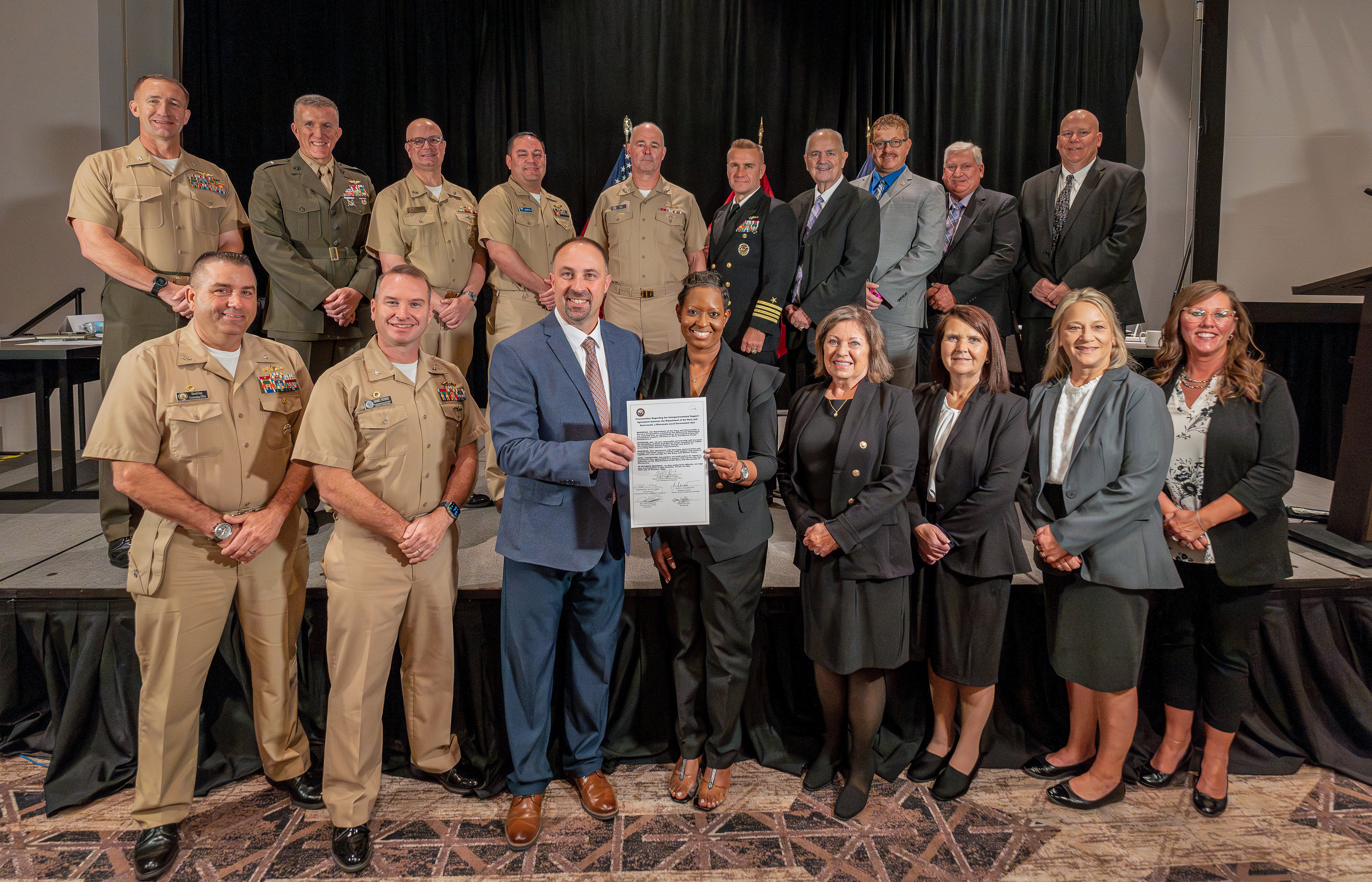 A group of civilians and Marines posing with the new Intergovernmental Support Agreement partnership paper.