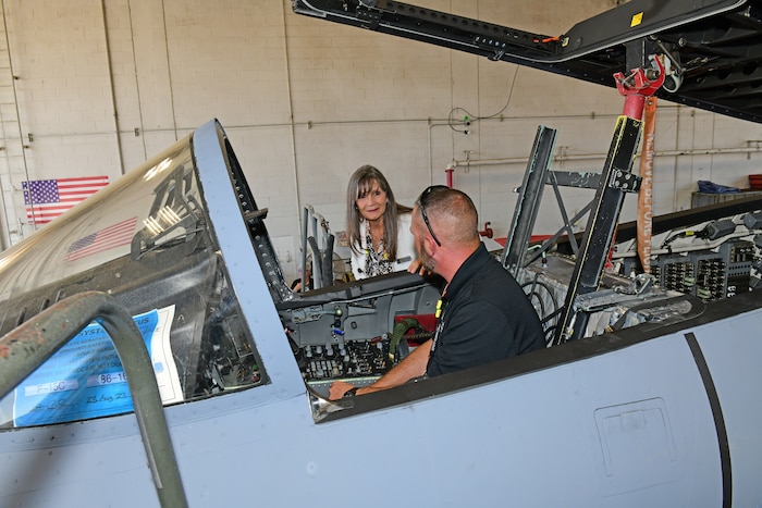 Photo shows a woman talking to a man who is sitting inside the cockpit of an aircraft