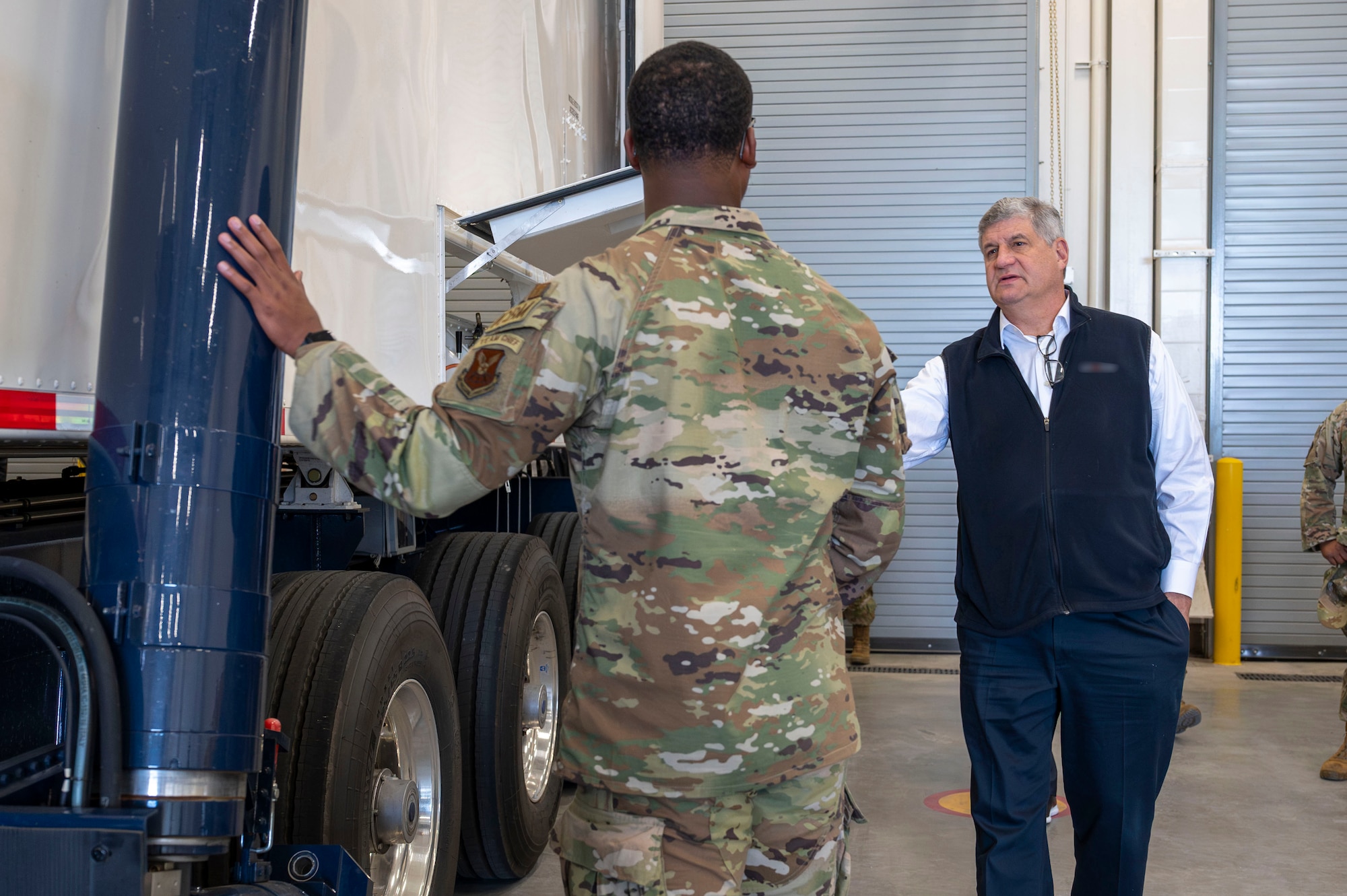An Airman speaks to a man about a military vehicle.