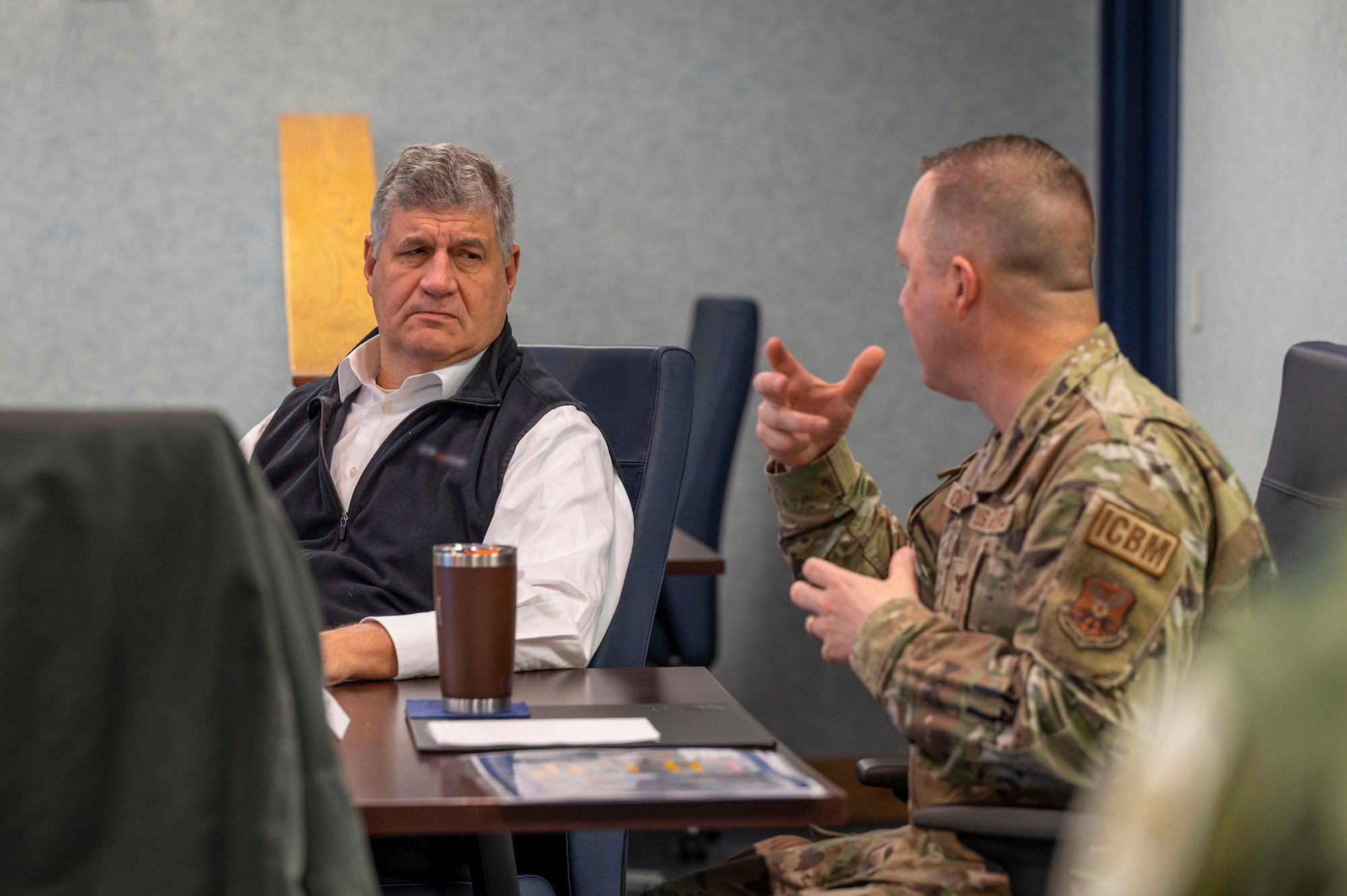 A man briefs another man at a conference table.
