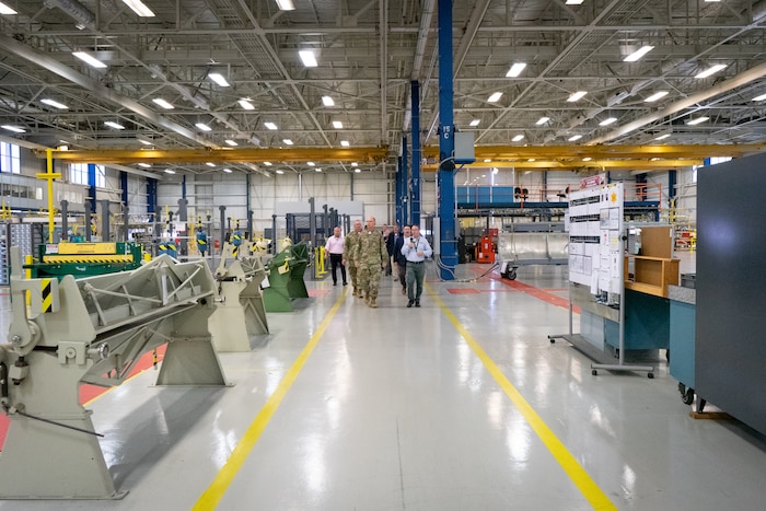 Photo shows group of people walking along lines of machines